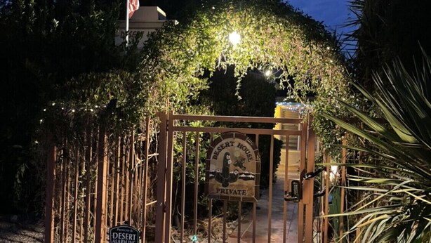A gated entrance to a private desert house with a stone lion statue at the base.