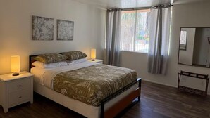 A bedroom with a bed, two bedside lamps, a window with curtains, and a mirror on the wall.