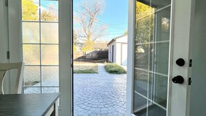 A modern kitchen with a dining table, a sliding glass door leading to a paved outdoor area, and a view of a residential neighborhood.