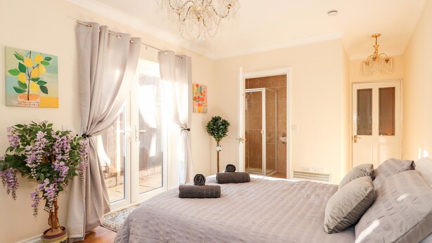A bedroom with a large bed, a chandelier, a shower room, and a door leading to an outdoor area. - 4 Dorothy Avenue (Skegness)