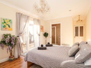 A bedroom with a large bed, a chandelier, a shower room, and a door leading to an outdoor area. - 4 Dorothy Avenue (Skegness)
