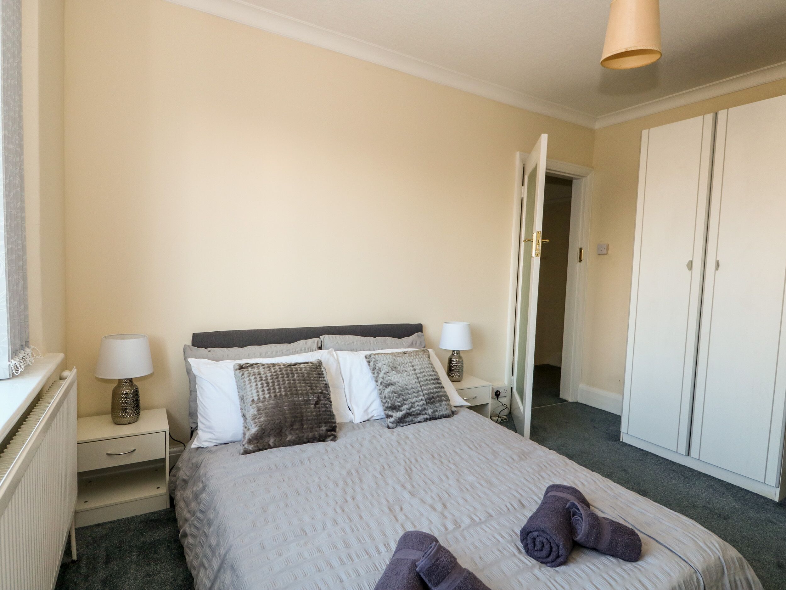 A neatly arranged bedroom with a bed, bedside tables, a wardrobe, and a door leading to another room.