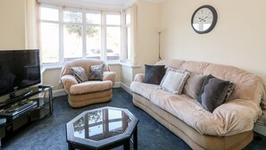 A living room with a beige sofa, a smaller armchair, a glass coffee table, and a flat-screen TV. - 4 Dorothy Avenue (Skegness)