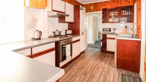 A kitchen with wooden cabinets, a stove, a microwave, and a sink. - 4 Dorothy Avenue (Skegness)