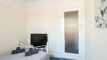 Un dormitorio con cama, televisor sobre un mueble, puerta con panel de vidrio esmerilado y un cuadro en la pared.