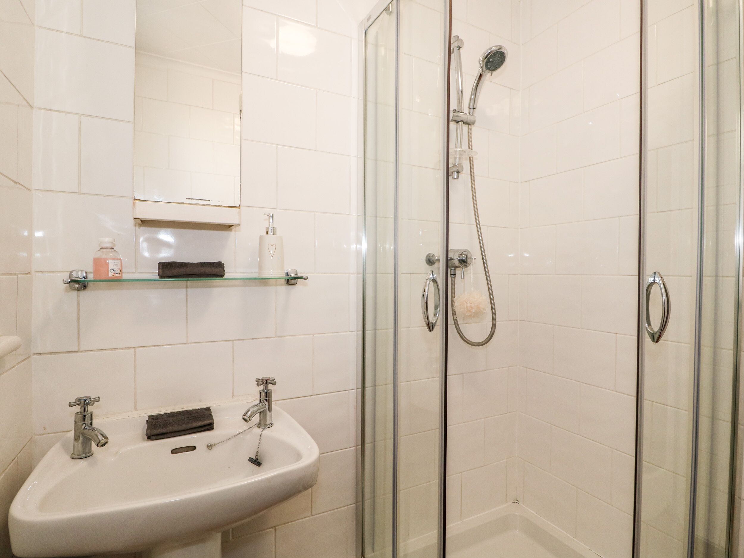 Ein Badezimmer mit einer Duschkabine, einem Waschbecken mit Spiegel und einer Ablage für Toilettenartikel.