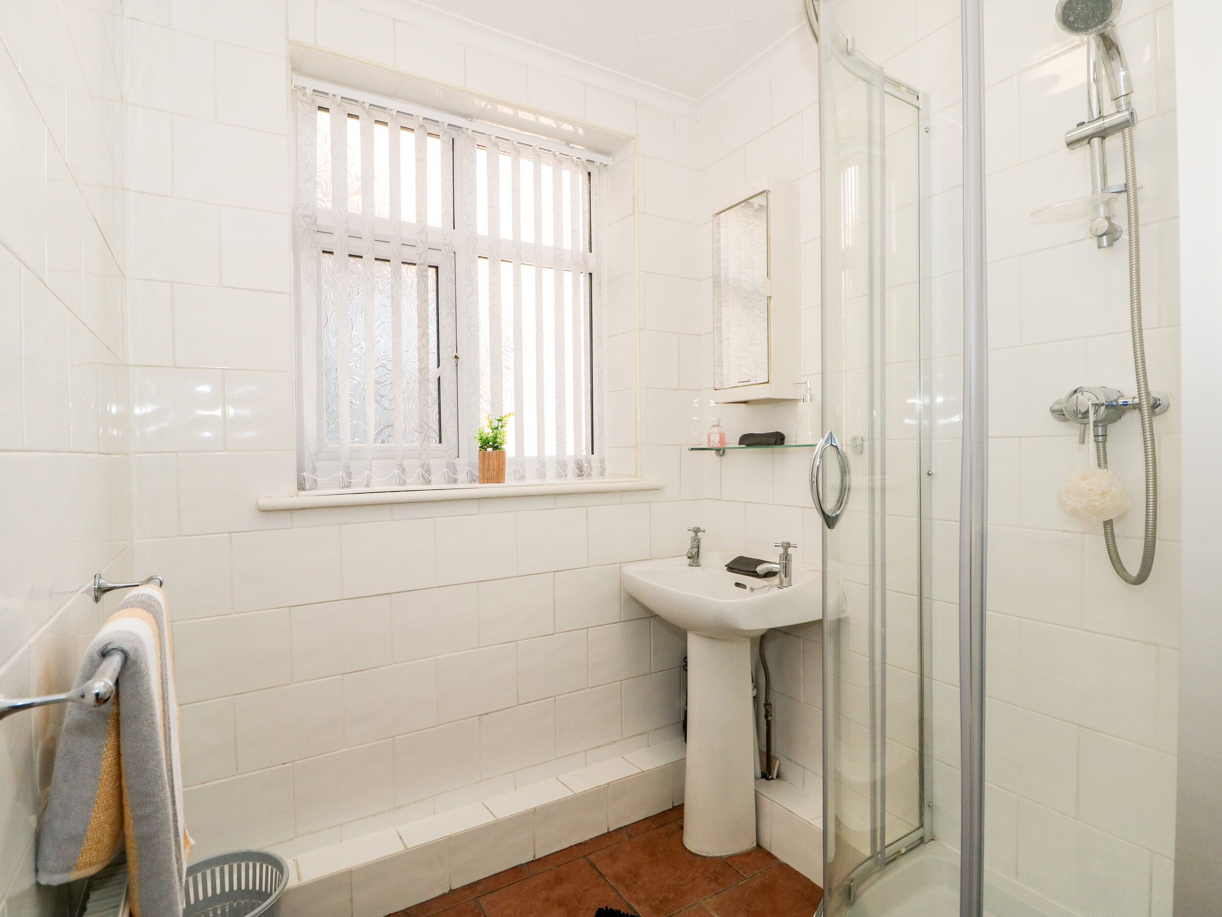 A bathroom with a window, a sink, a shower, and a towel rack.