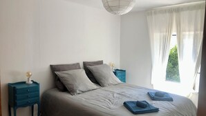 Een slaapkamer met een groot bed, twee nachtkastjes, een hanglamp en een raam met dunne gordijnen.