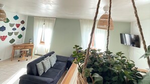 Een woonkamer met een bank, een televisie, een bureau en een hangplant.