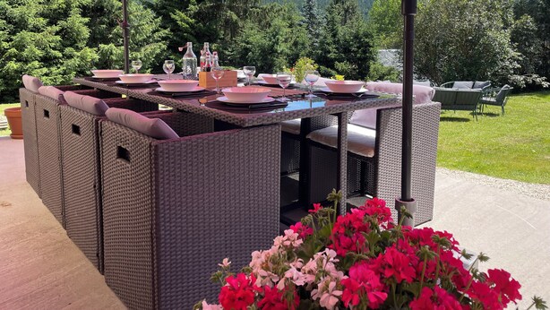 Een terras met rieten meubilair en een rode parasol.