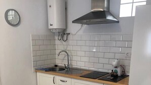Une cuisine compacte avec des meubles blancs, une hotte de cuisinière en acier inoxydable, un évier et une table en bois.