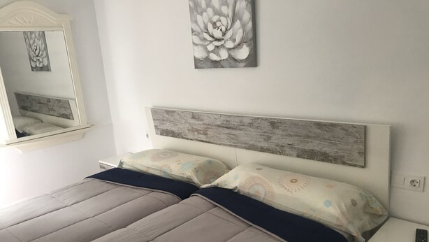 Une chambre à coucher comprenant un lit, des tables de chevet, un miroir et un tableau représentant des fleurs accroché au mur.