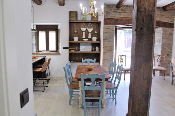 A dining area with a wooden table and blue chairs, a chandelier, and a stone wall. - ESTRELLA DEL SIL COTTAGE (Corbon del Sil)