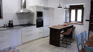 Et moderne køkken med hvide skabe, et rustfrit stål emfang, indbygget ovn og en central ø med barstole.