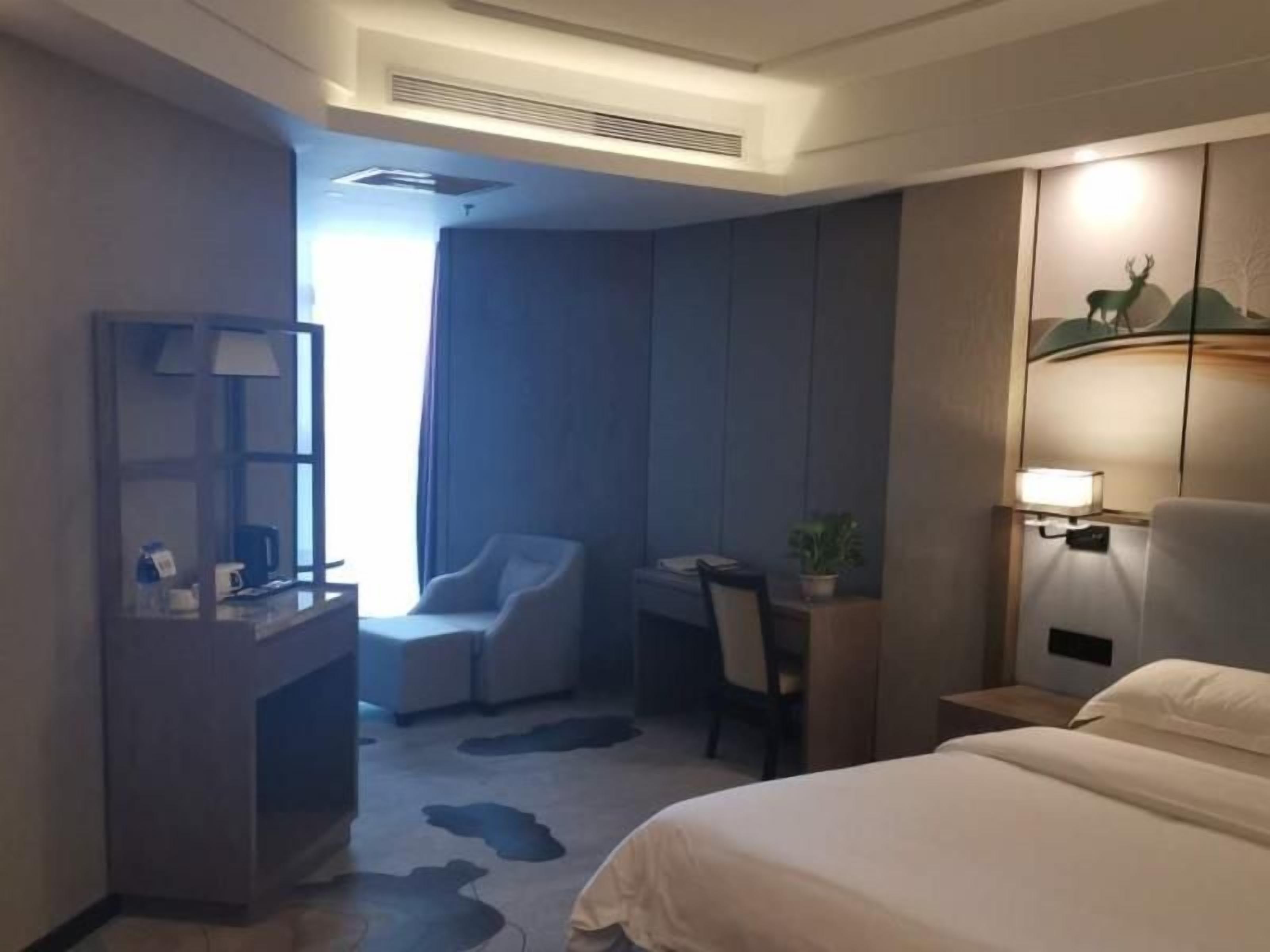A hotel room with a bed, a desk, a chair, a small table, and a nightstand.