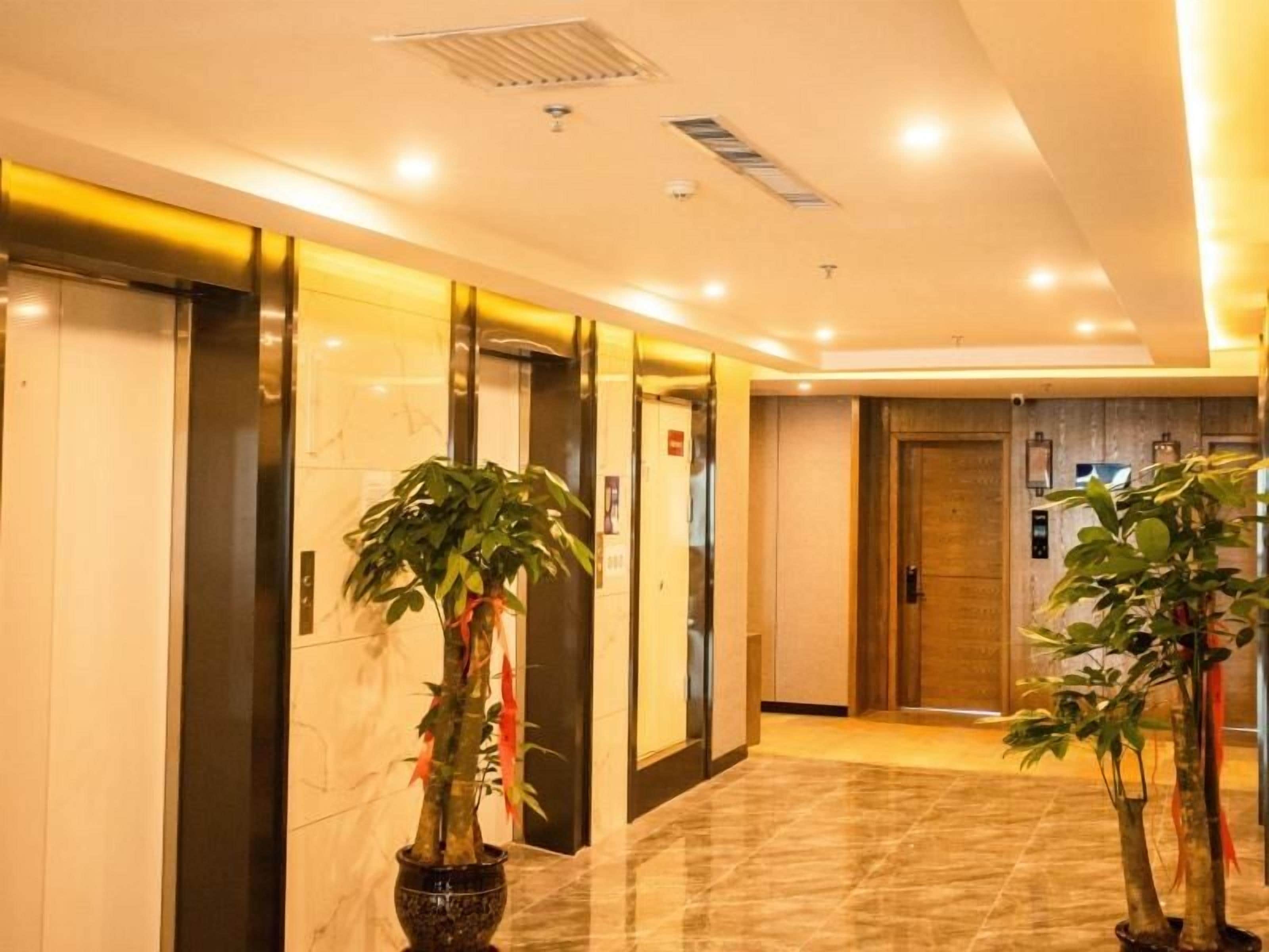 A hotel lobby with elevators, potted plants, and a marble floor.