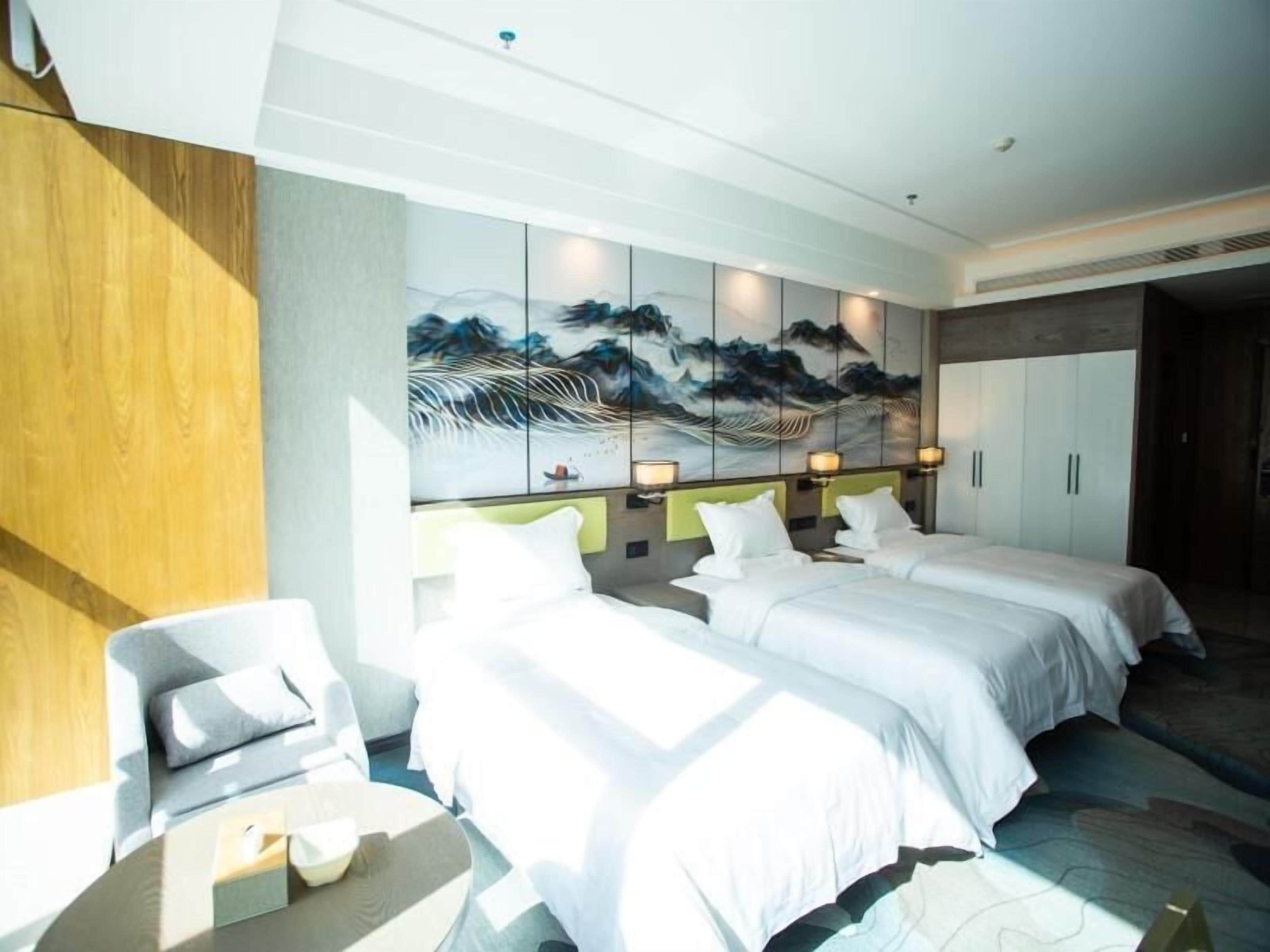 Quarto de hotel com duas camas, um sofá, um quadro na parede e um painel de madeira à esquerda.