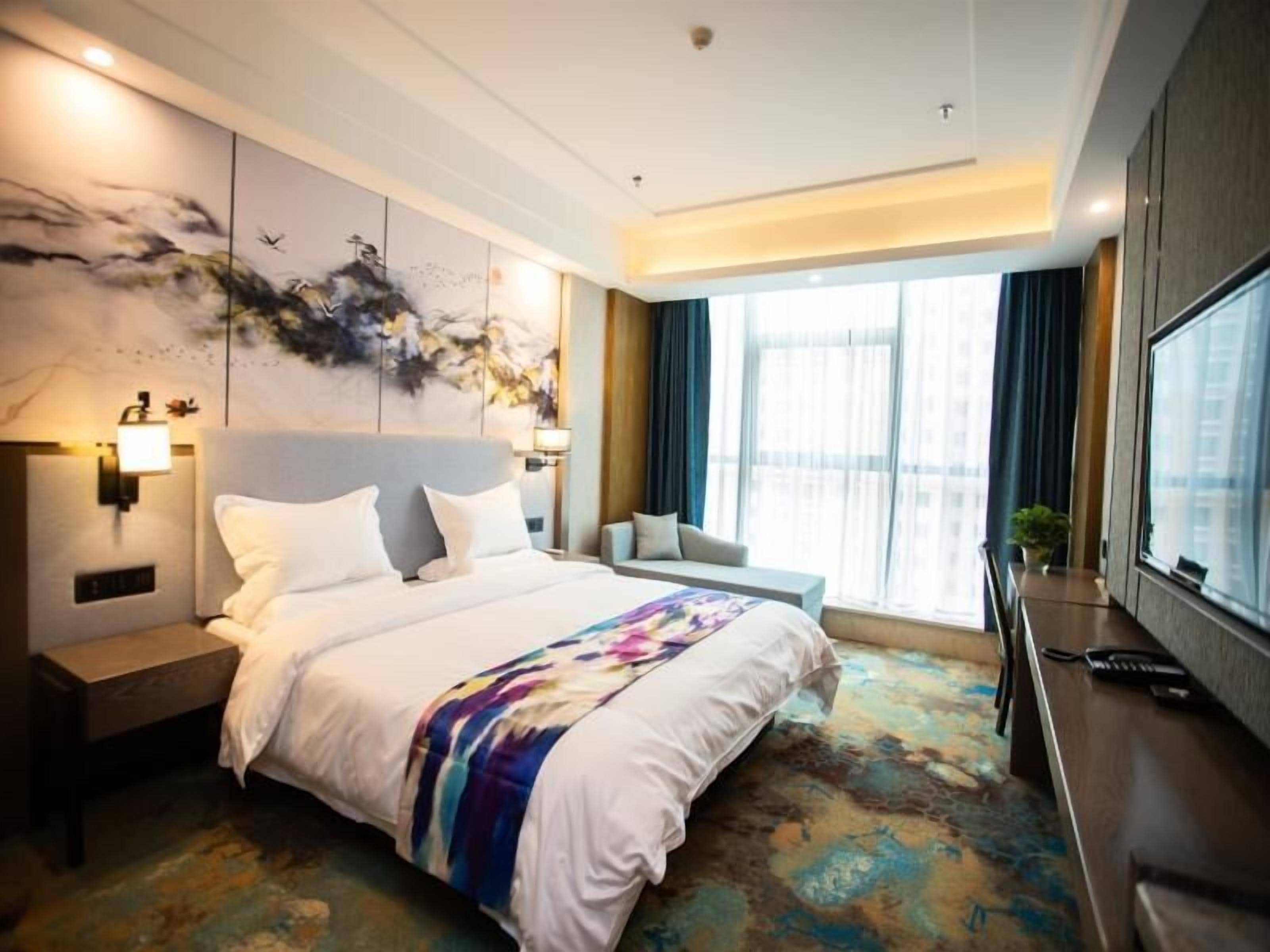 A modern hotel room with a large bed, a desk, and a window with curtains.