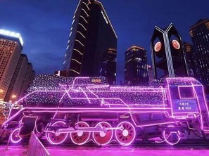 Um trem com luzes néon numa paisagem urbana noturna.