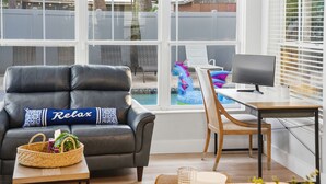 A modern living room with a leather sofa, a wooden desk, and a view of a swimming pool.