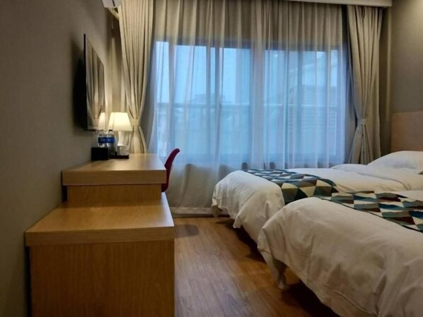 Ett hotellrum med ett skrivbord i trä, två sängar, en tv och ett fönster med gardiner.