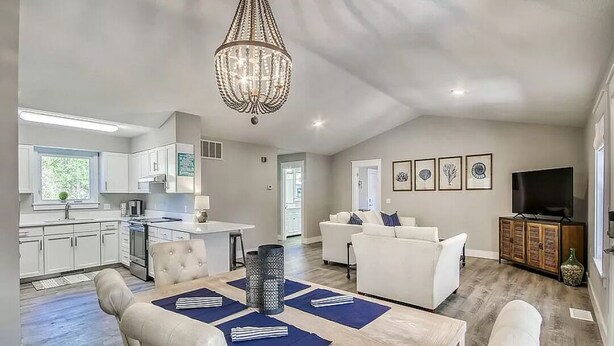 A spacious living area with a dining table, white sofas, a chandelier, and a television.