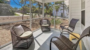 A sunlit room with large windows, wicker chairs, and a flat-screen TV.
