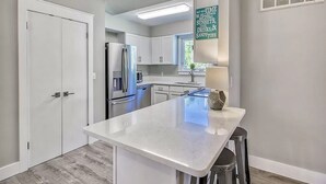 A modern kitchen with white cabinets, a central island, stainless steel appliances, and a window with a view.