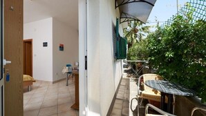 A small patio area with a table and chairs, a door leading to an interior room, and a green fence with plants.
