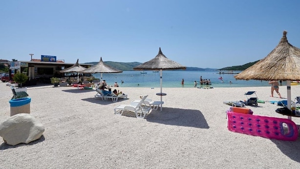 A beach with white lounge chairs, thatched umbrellas, and a clear view of the sea. - Apartment in Seget Vranjica with Seaview, Balcony, Air condition, WIFI (5052-3) (Seget Vranjica)