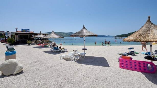 A beach with white lounge chairs, thatched umbrellas, and a clear view of the sea. - Apartment in Seget Vranjica with Seaview, Terrace, Air condition, WIFI (5052-5) (Seget Vranjica)