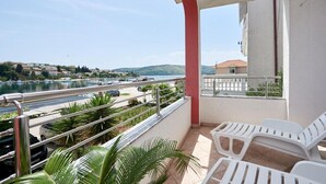 A balcony with white plastic chairs, a view of a body of water, and a road with cars. - Apartment in Seget Vranjica with Seaview, Terrace, Air condition, WIFI (5052-5) (Seget Vranjica)