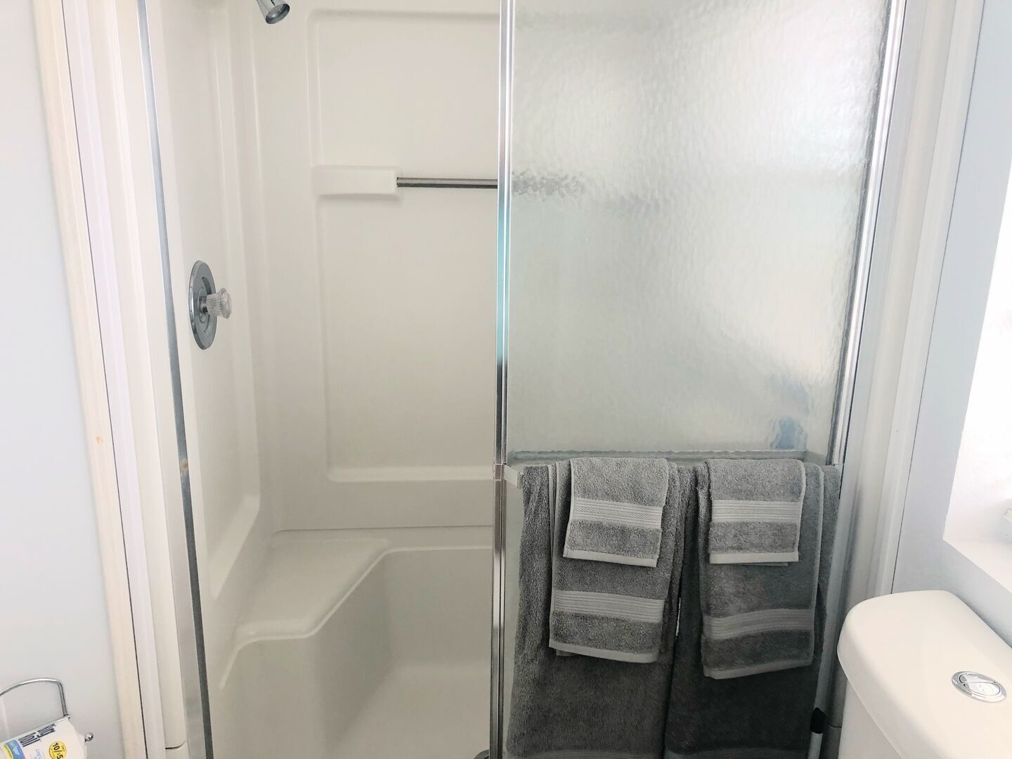 Un bagno con cabina doccia in vetro, un water bianco e asciugamani su un portasci.