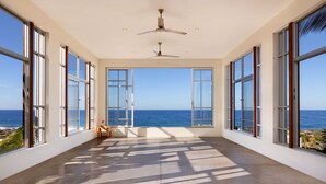 A room with large windows, a ceiling fan, and a view of the ocean. - Topia Sunset Suite All Inclusive (El Pescadero)