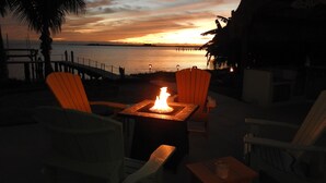A sunset view from a deck with two chairs and a table with a fire.