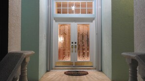 A hallway leading to a double door with a glass panel, a doormat, and stone balustrades on either side.