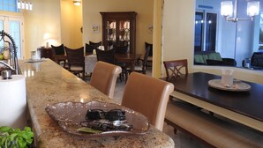 A dining area with a granite countertop, chairs, a wooden cabinet, and a window with a view.