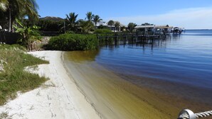 A beach with clear water, a rope barrier, and a dock with buildings in the background.