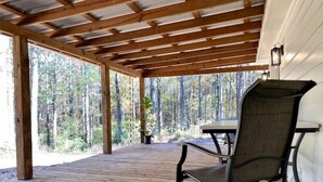 Un espacio al aire libre techado con una terraza de madera, una sola silla y una mesa.