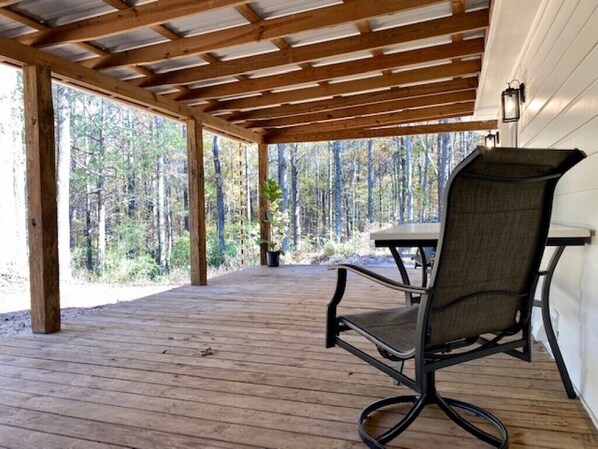 A covered outdoor area with a wooden deck, a single chair, and a table.