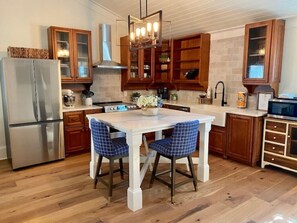 A kitchen with wooden cabinets, a stainless steel refrigerator, a white dining table with blue chairs, and a pendant light.