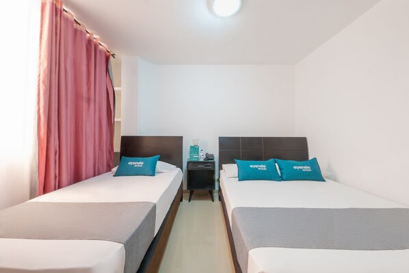 Habitación de hotel con dos camas, cada una con un cojín que dice 'ayenda hotels'.