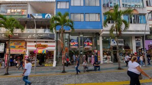 A busy street with palm trees, shops, and people walking. - Ayenda Ambeima (Ibagué)