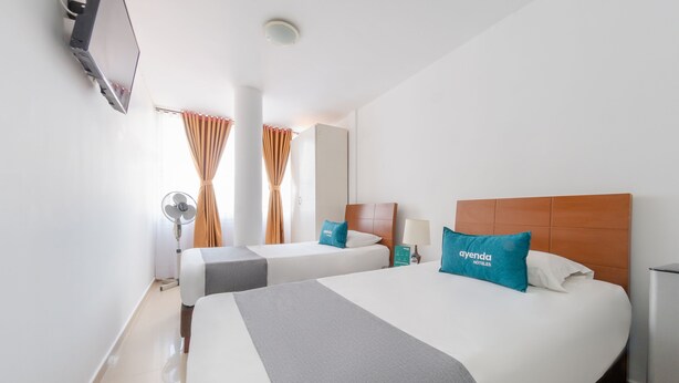 A hotel room with two beds, a TV mounted on the wall, a mirror, and a window with curtains. - Ayenda Ambeima (Ibagué)