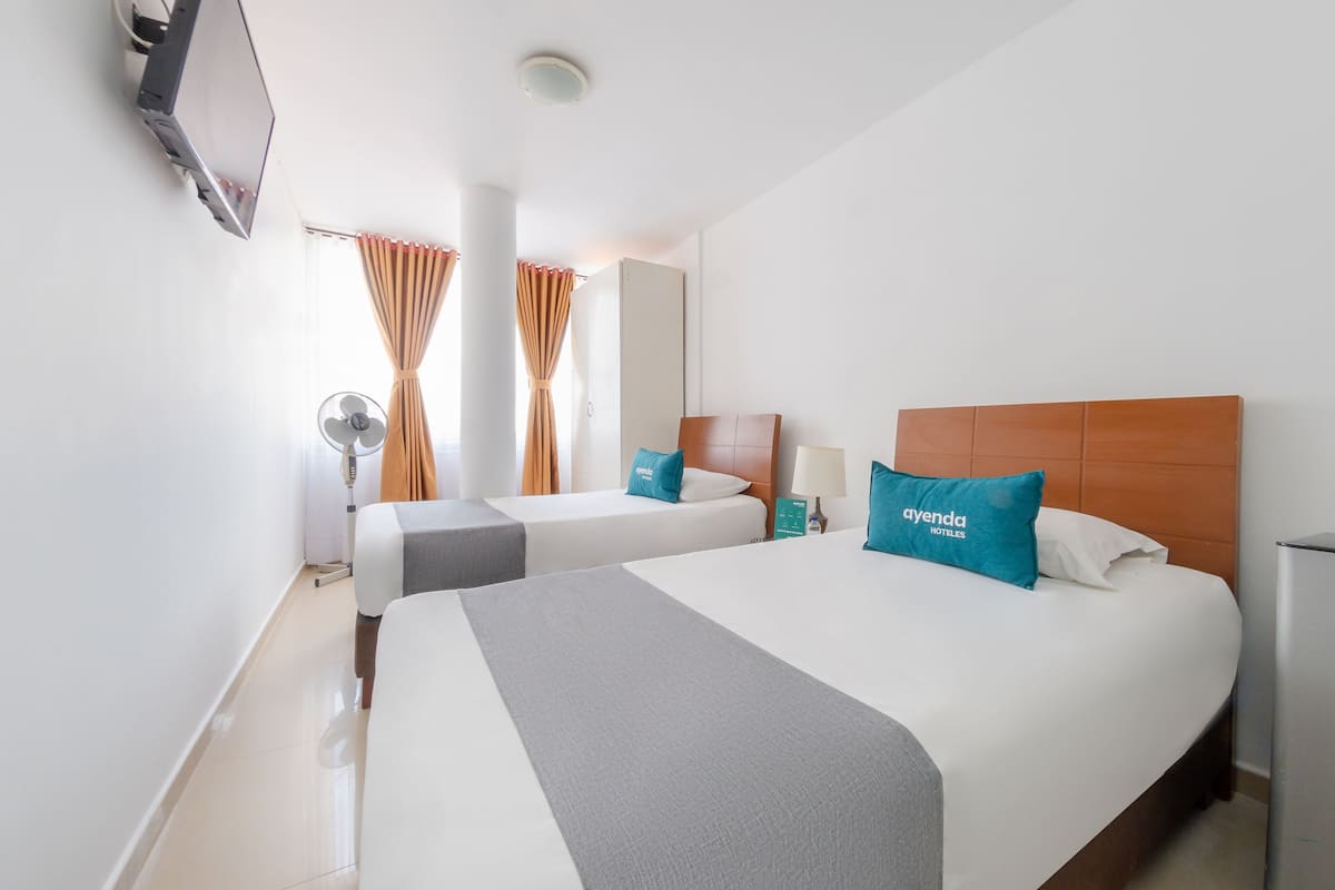A hotel room with two beds, a TV mounted on the wall, a mirror, and a window with curtains.