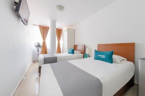 Una habitación de hotel con dos camas, un televisor montado en la pared, un espejo y una ventana con cortinas.