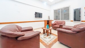 A spacious room with leather sofas, a flat-screen TV, a window with blinds, and a small table with a water bottle. - Ayenda Ambeima (Ibagué)