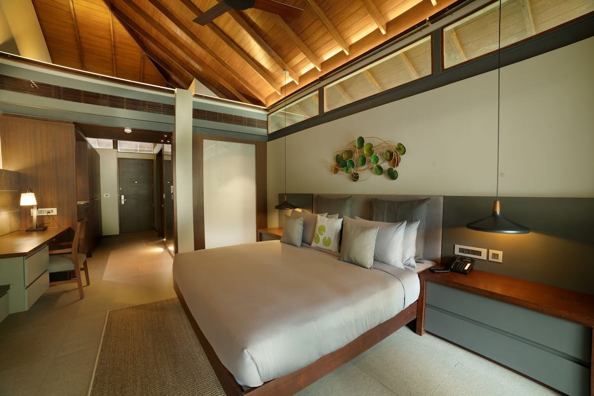 Quarto de hotel moderno com uma cama grande, mesa de cabeceira e escrivaninha com abajur.