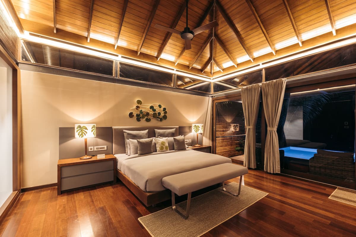 Quarto moderno com teto de madeira, uma cama grande, mesas de cabeceira e vista para o exterior.
