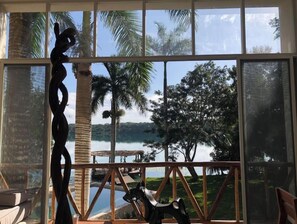 A room with a large window overlooking a lake, palm trees, and a wooden deck.